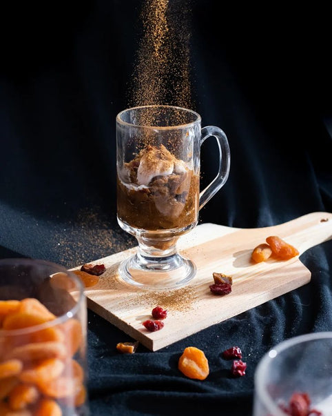 Latvian rye bread dessert in a clear handled glass on a wooden board, with dried fruit and a dusting of spice.