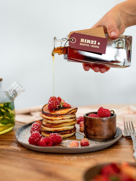 BIRZĪ meadowsweet syrup poured over pancakes and raspberries